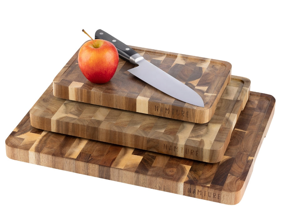 Drie Namture snijplanken van acaciahout in verschillende maten, gestapeld met een mes en appel op de bovenste plank.