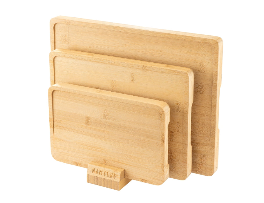Drie bamboe snijplanken van Namture in verschillende maten, rechtop geplaatst in de bijbehorende bamboe houder.