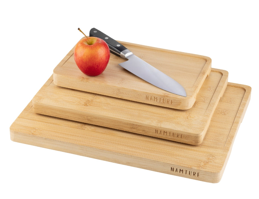 Drie bamboe snijplanken van Namture in verschillende maten, gestapeld met een mes en appel op de bovenste plank.