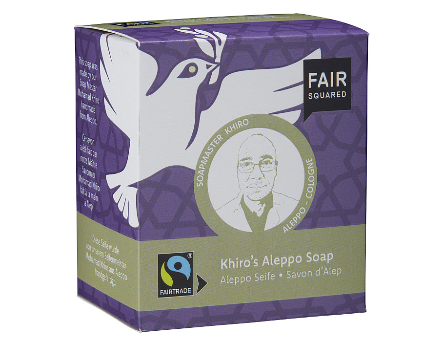 Fair Squared Khiro’s Aleppo Soap in paarse en groene verpakking met illustratie van een vredesduif en een portret van Soapmaster Khiro; fairtrade Aleppo-zeep.